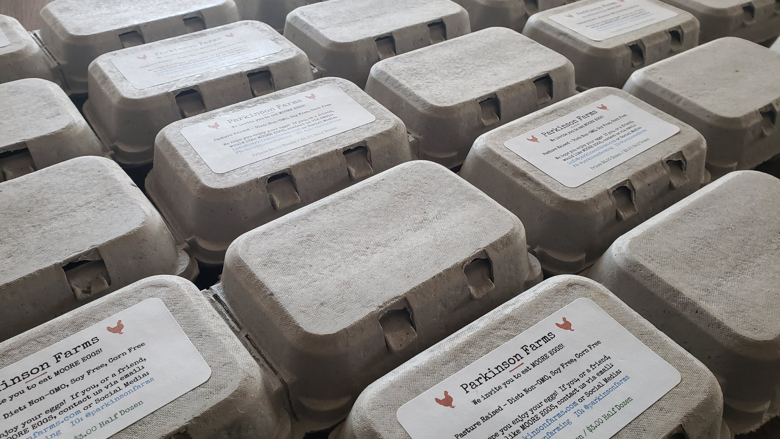 Cartons of eggs from Parkinson Farms, featuring eco-friendly packaging and labels highlighting non-GMO, soy-free, and corn-free diets for the chickens. The image showcases the farm's commitment to quality and sustainable practices.