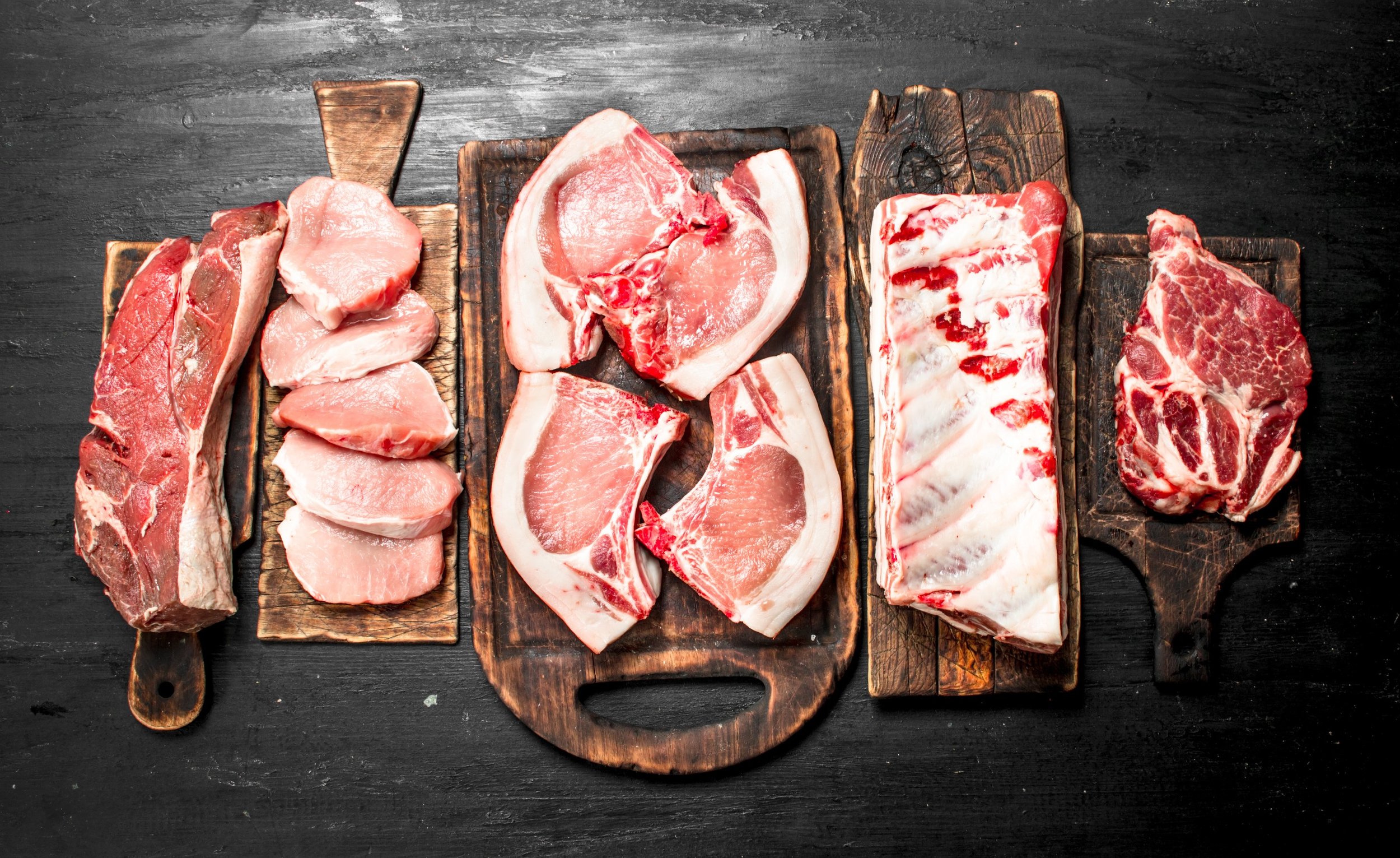 Variety of fresh meats displayed on wooden cutting boards, including pork chops, pork loin, ribs, and beef cuts, set against a dark background. Ideal for showcasing meat preparation or butchery.